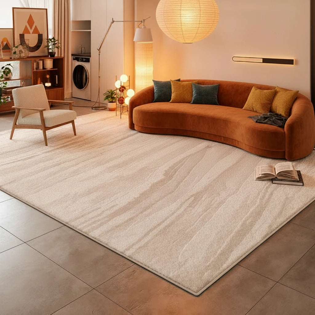 A large rectangular area rug in a light beige and off-white marble-like pattern, shown in a modern, minimalist living room with a white sofa, gray tiled floor, and a black armchair.