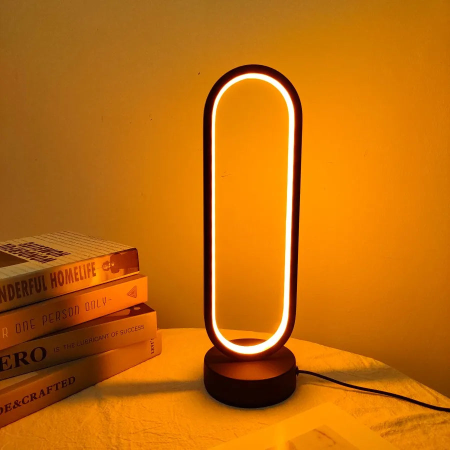 Modern table lamp with a warm glow on a surface with books underneath, against an orange wall.